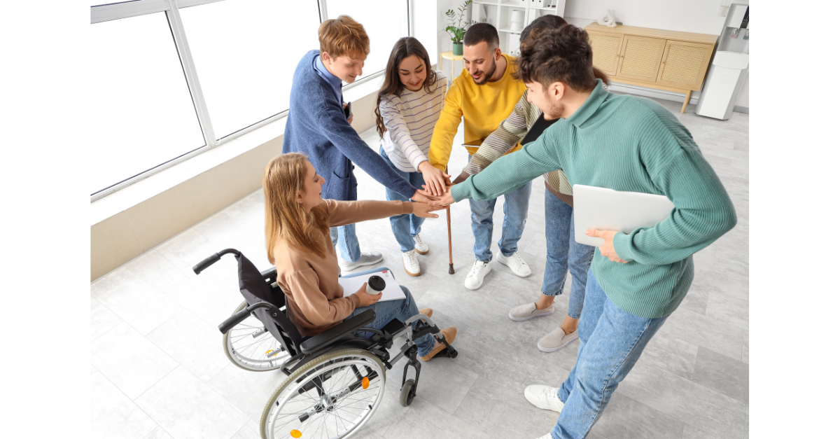 A group of people are all putting their hands in the middle ready to life up and one lady is in a wheelchair.