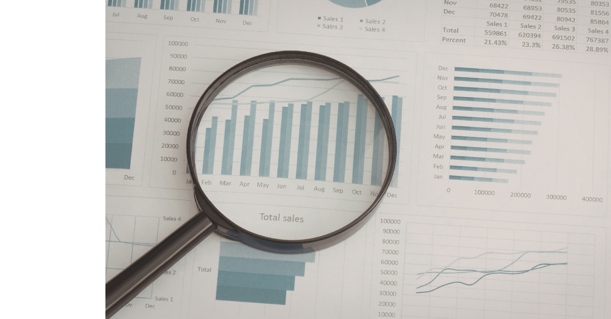 There is paper laid out with graphs and charts on and a magnifying glass across one of them.