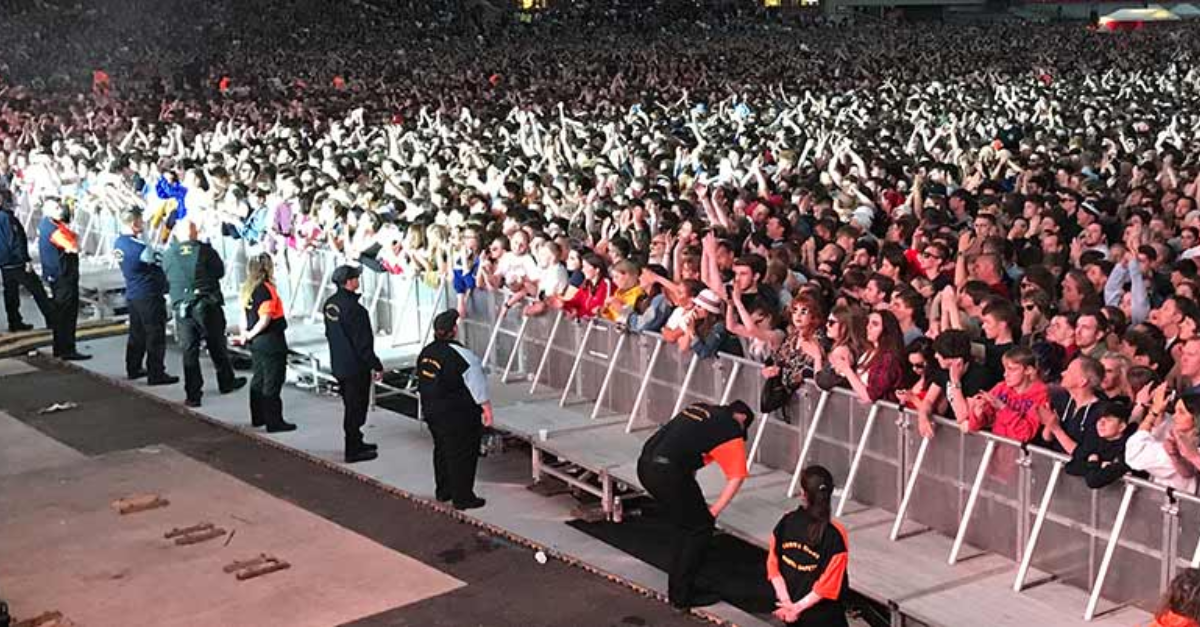There is a large crowd and there is a big team of event staff on the other side of a barrier on a stage.