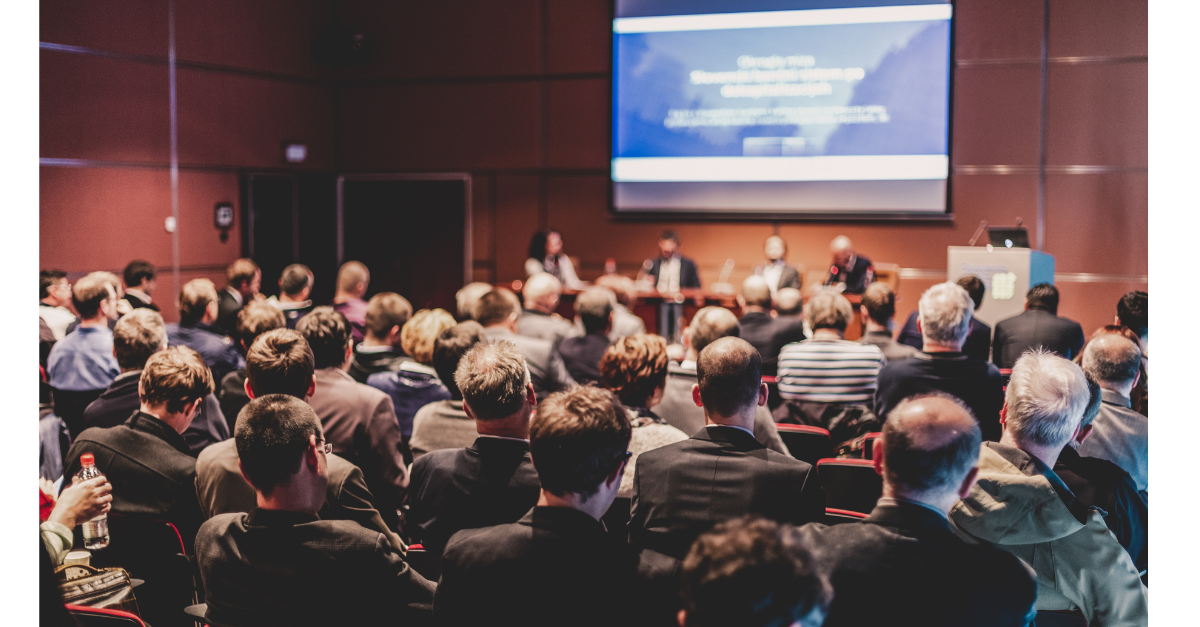There are a group of people sat in front of a large screen ready for a presentation.