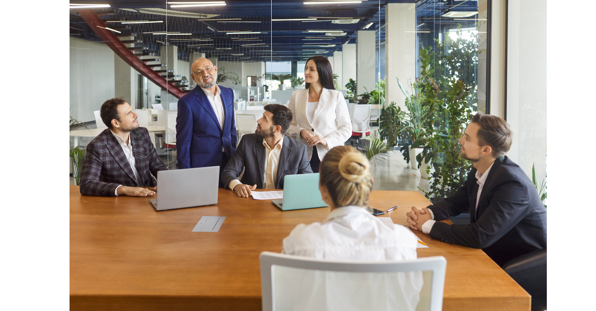 A team of people are in an office room with laptops and talking.