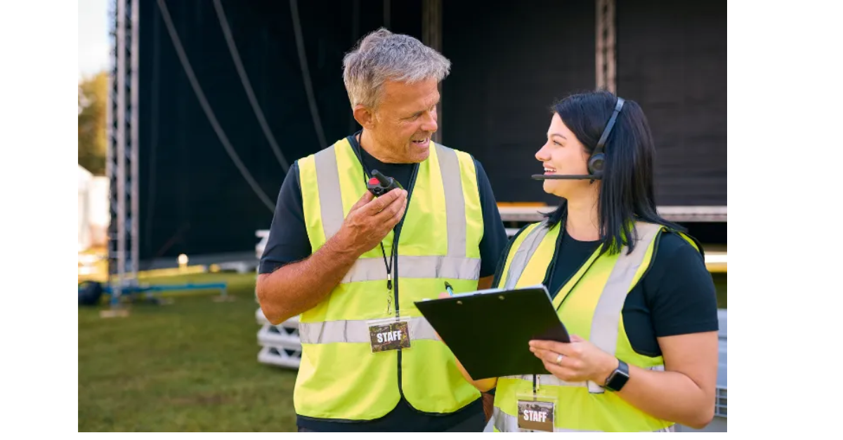 Two event staff are speaking, one on the walkie talkie and one on a headset with a tablet wearing hi-vis.