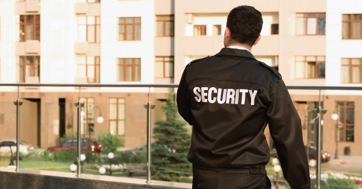 A security man in his uniform is looking over a balcony at houses across the road.