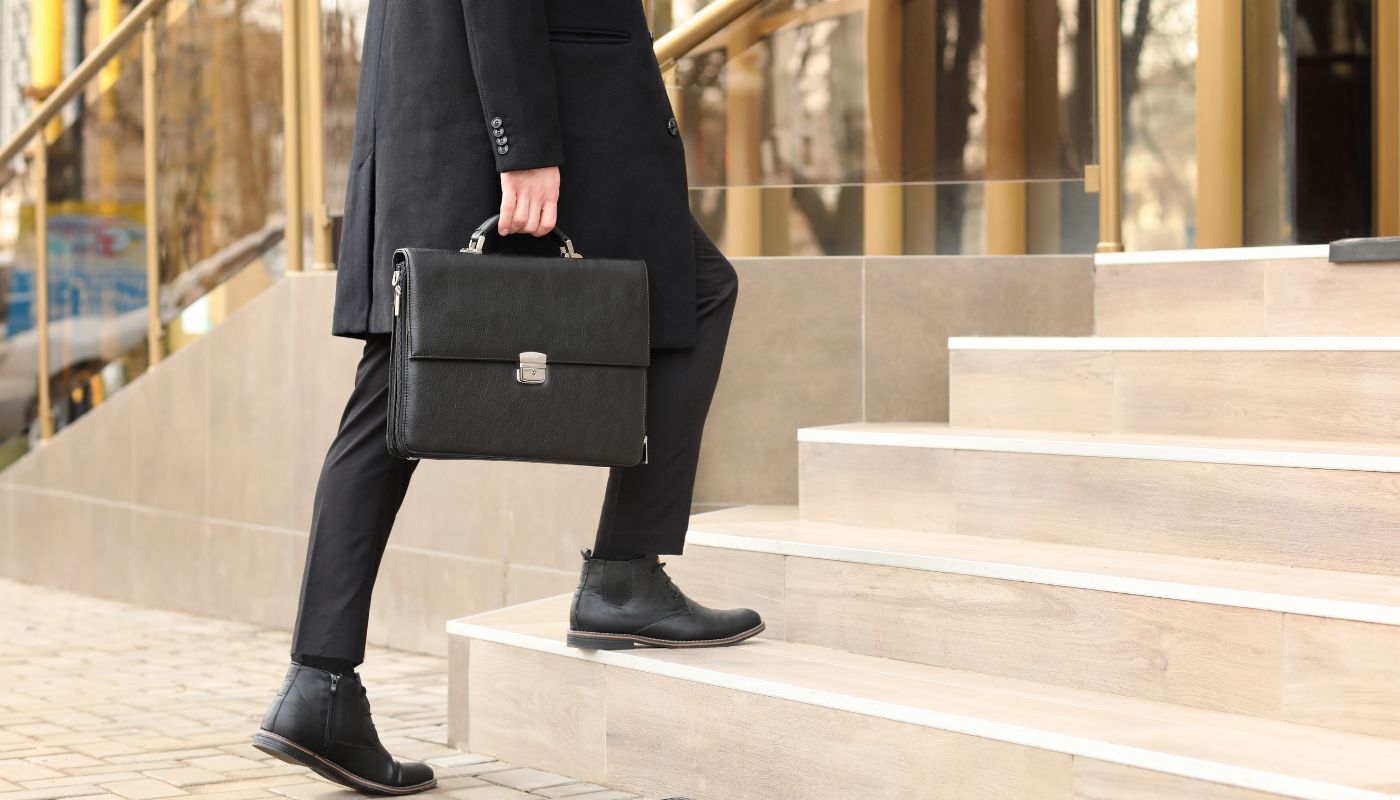 A man is walking up the stairs to a building carrying a briefcase.