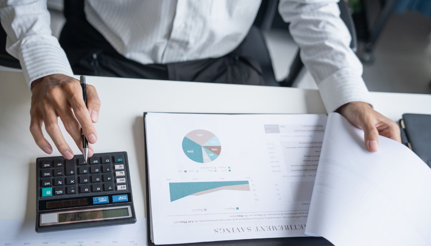 A business man is reviewing documents and clicking buttons on a calculator with a pen in hand.