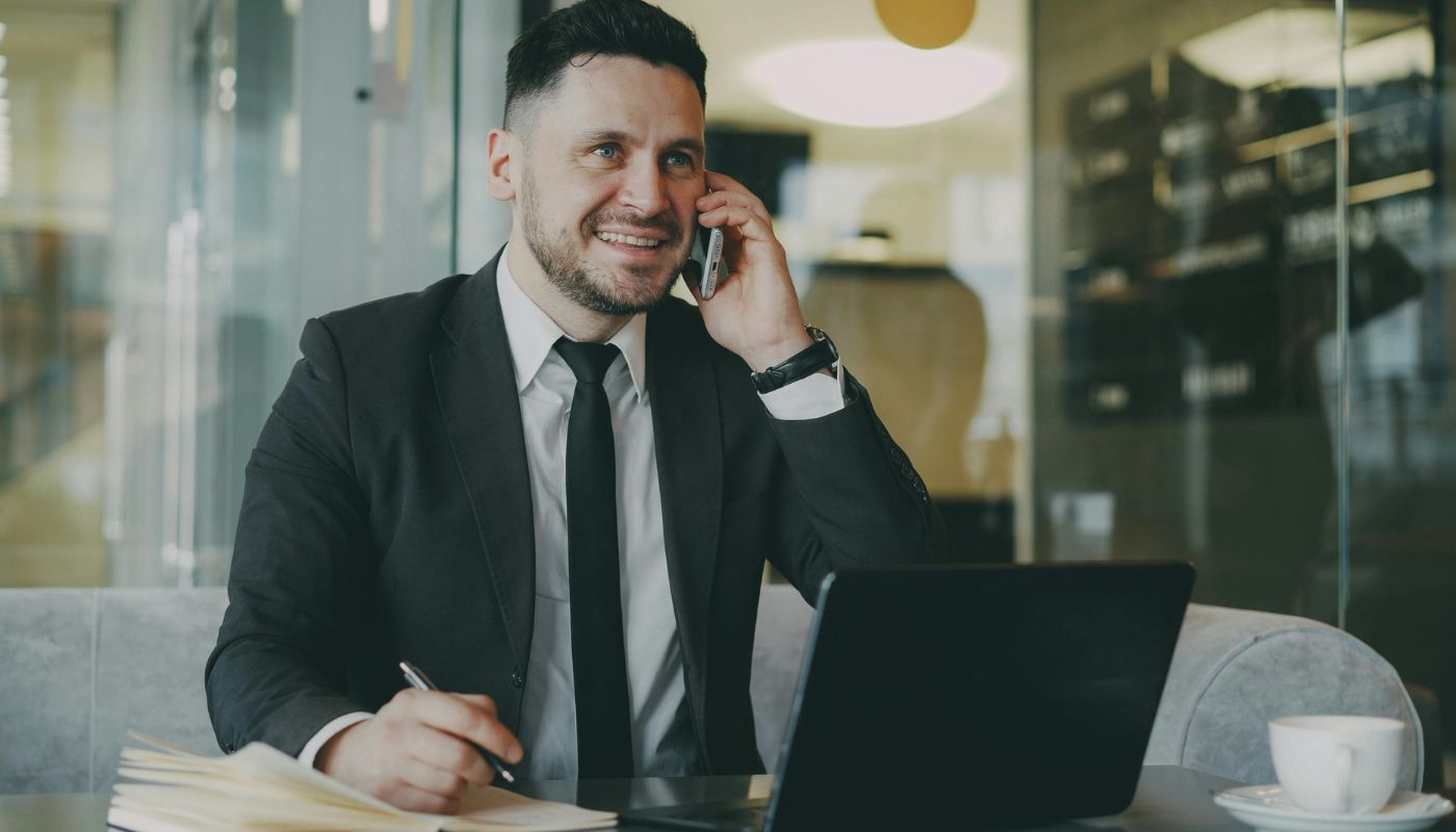 Business man on the phone with laptop, notepad and pen in hand.