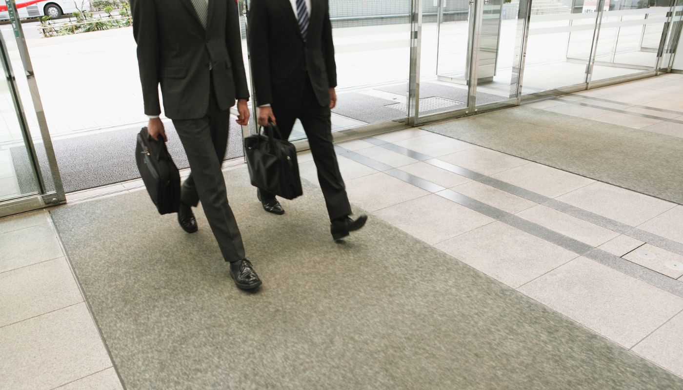 Two men are entering an office building walking with their briefcases.