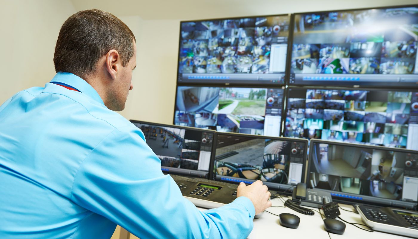 A man is in a control room operating the CCTV on the many screens.