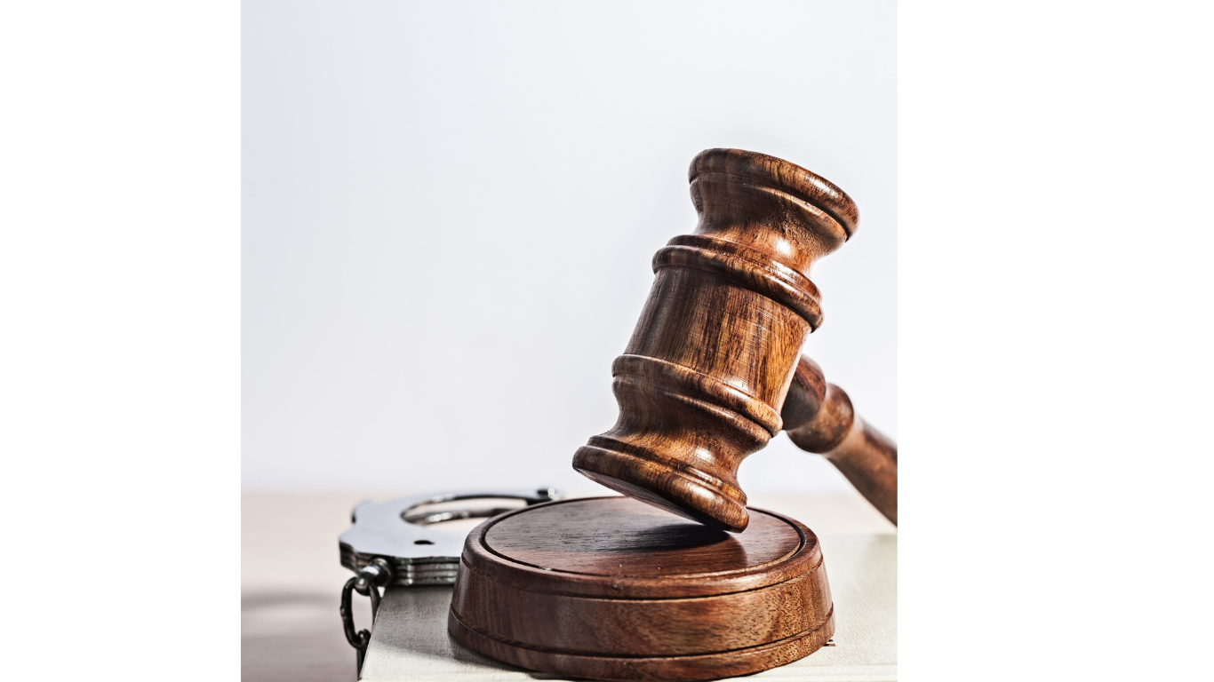 A wooden gavel is resting on a block with handcuffs in the background.