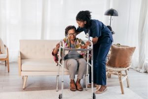 Nurse helping an elderly lady get up front the sofa onto her frame in her home.