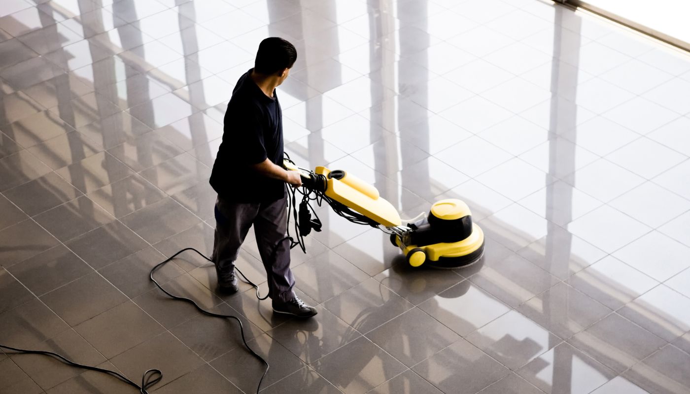 A cleaner is cleaning a public place floor, making it shiny using a buffer machine.