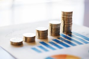 There is a piece of paper on a desk of a graph with coins stacked from lowest to highest on top of it.