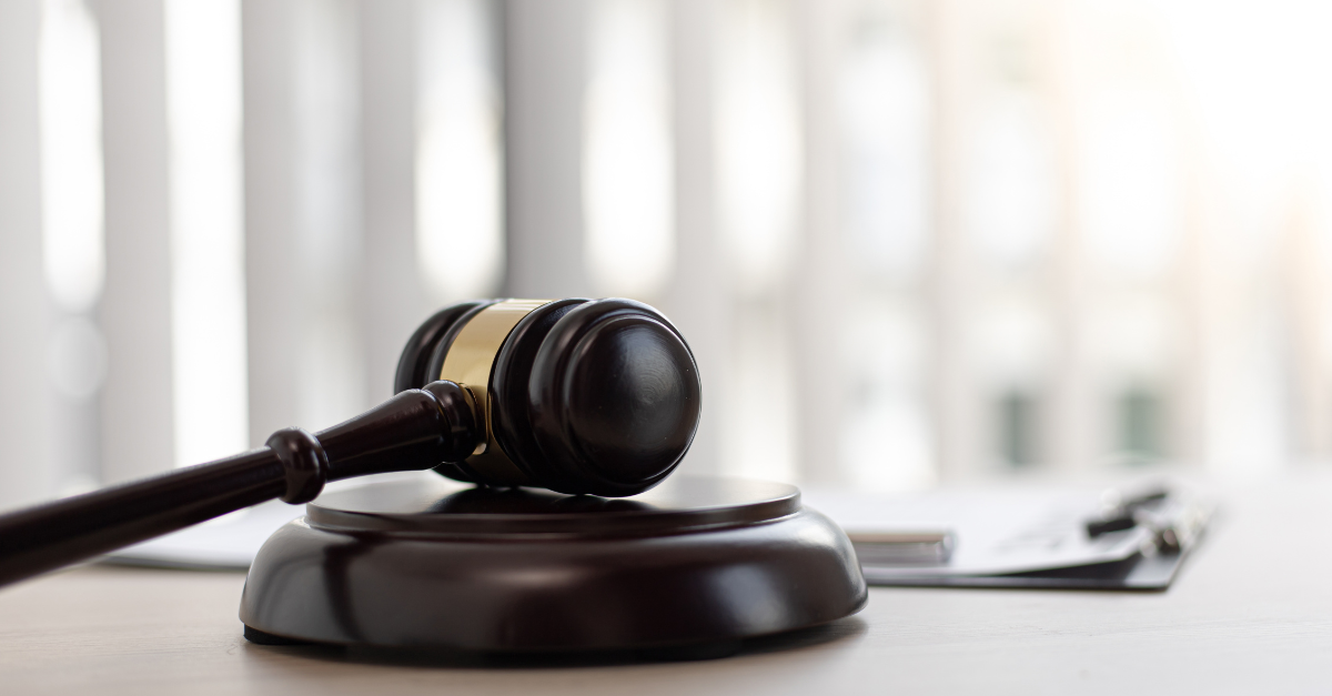 A gavel resting sideways on a wooden block with a clipboard behind it.