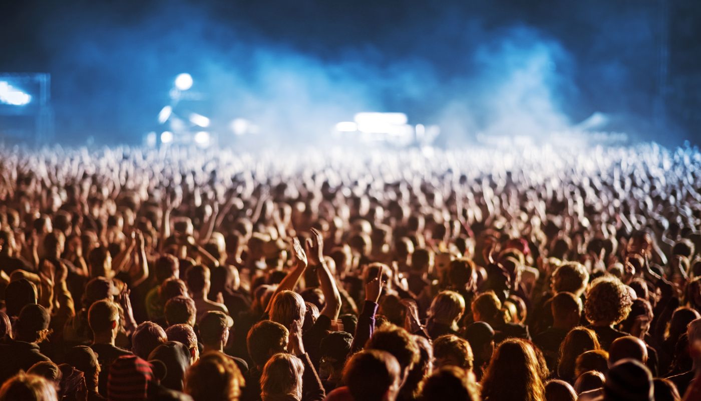 A massive crowd of people at an event with blue lights and smoke in the air.