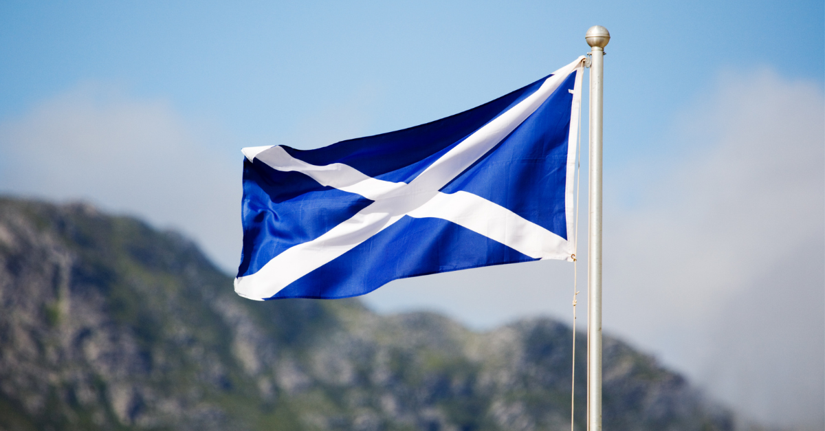 A Scottish flag on a pole in front of a view of a mountain or hill.