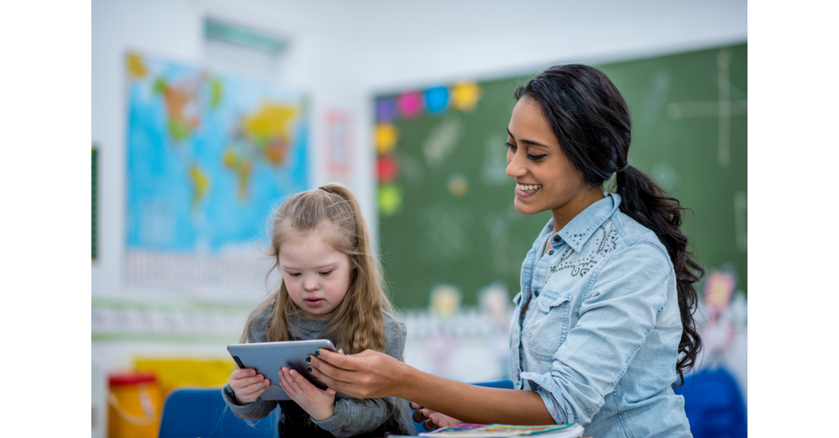 A teacher is smiling in a classroom with a child who is looking at a book.