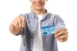 A women is smiling with a driving license in one hand and keys in another.