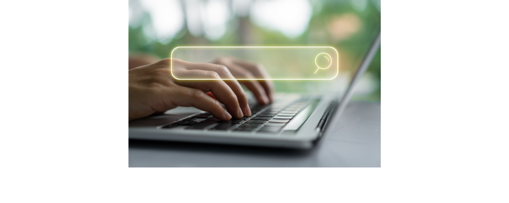 A laptop is open and it has a search bar with someone typing on the keyboard.
