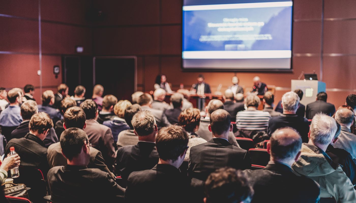 There are a group of people sat in front of a large screen ready for a presentation.