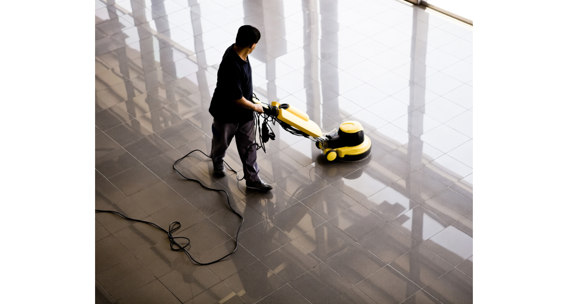A cleaner is cleaning a public place floor, making it shiny using a buffer machine.