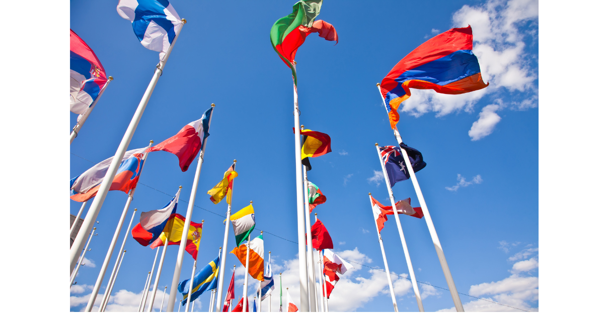 There are a variety of different countries flags on a flag poles high up outside.