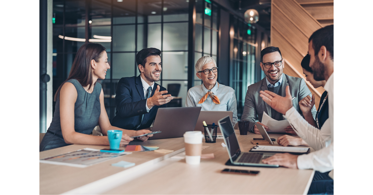 An office team in a meeting room discussing with laptop and coffees on show.