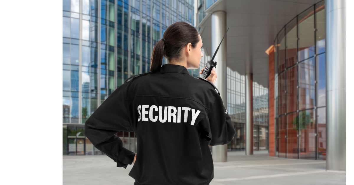 A women security guard is on her walkie talkie in front of buildings.