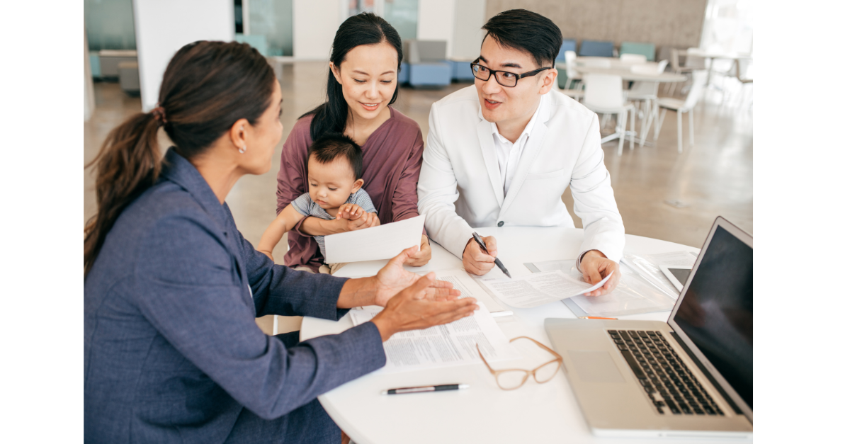 A family of three are sat at a desk with a member of staff having a discussion with a laptop open.