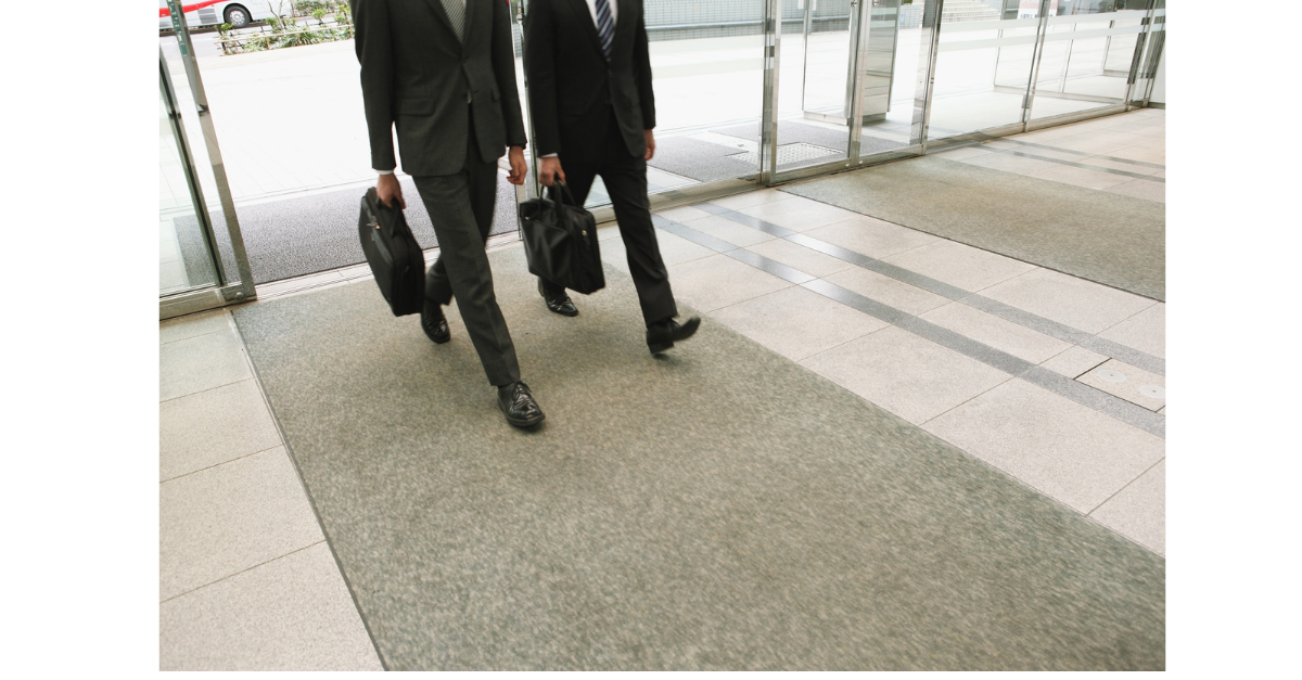 Two men are entering an office building walking with their breifcases.