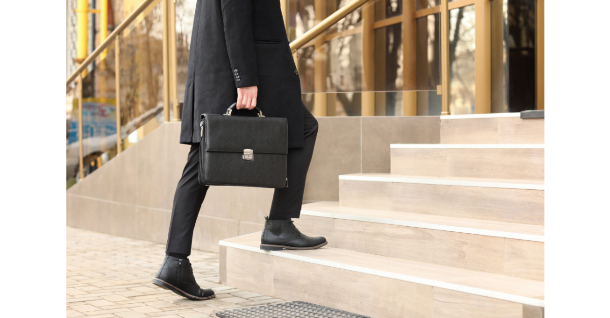 A man is walking up the stairs to a building carrying a breifcase.