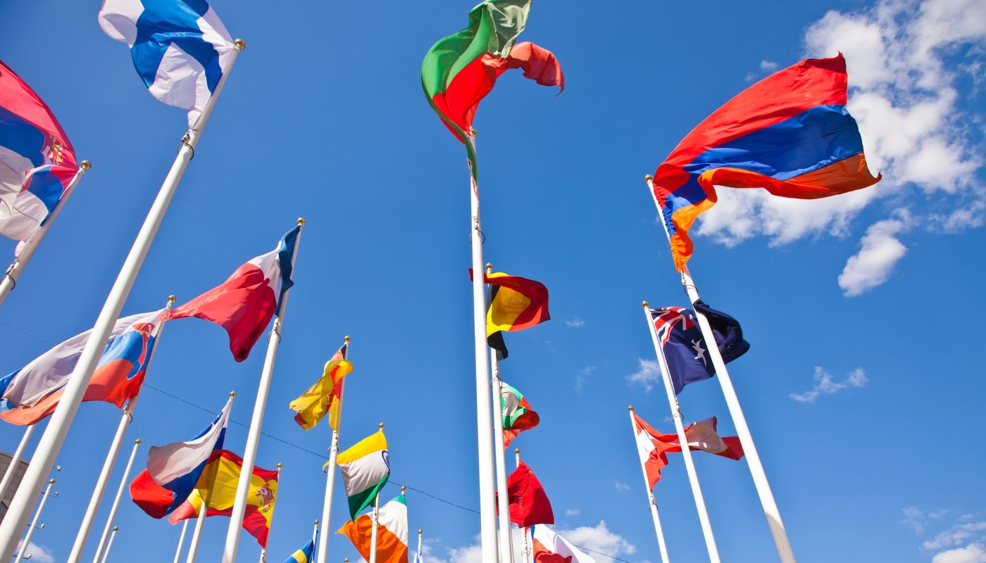 There are a variety of different countries flags on a flag poles high up outside.