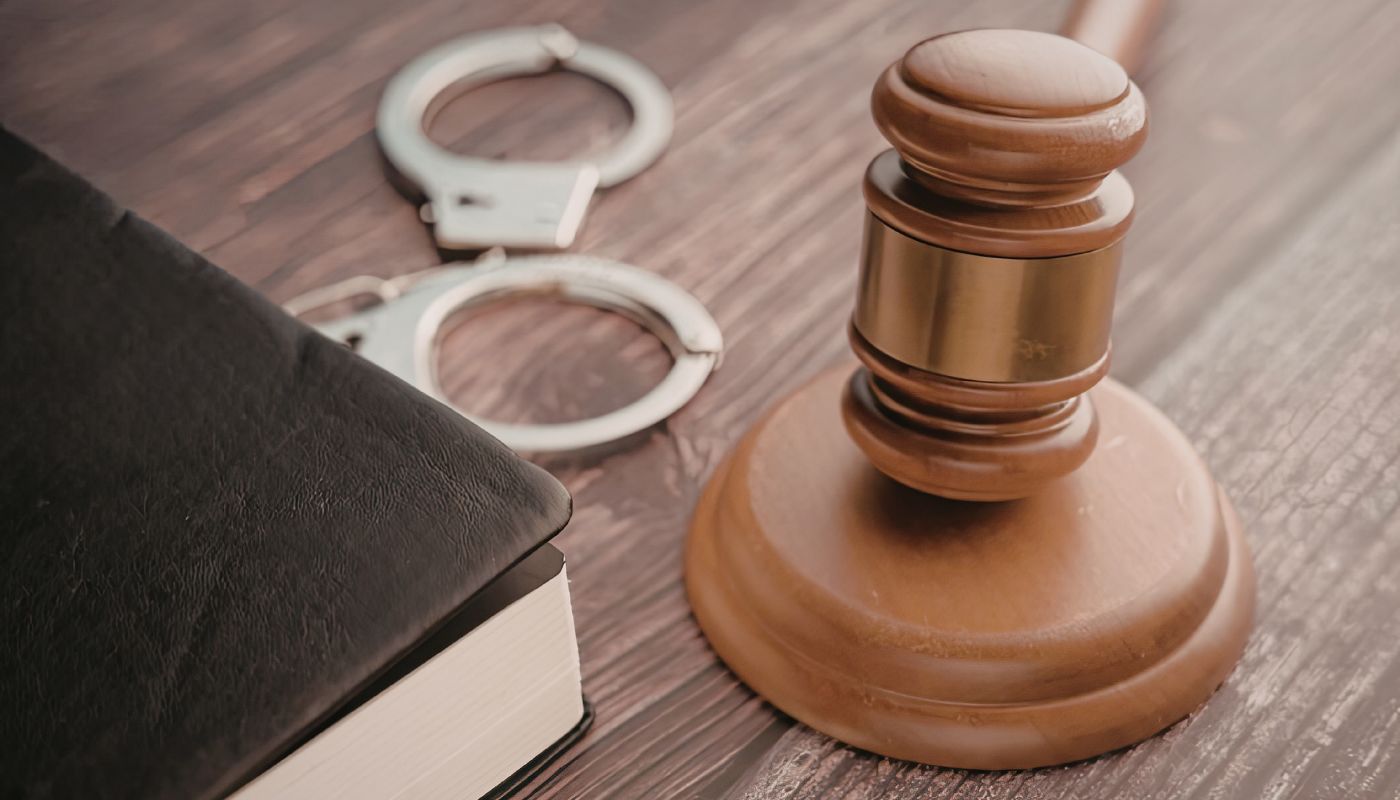 A gavel on a block with handcuffs and a book.