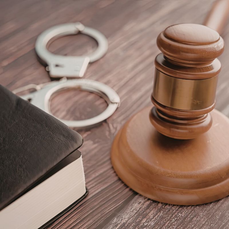 A gavel on a wooden block, handcuffs and a book all on a table next to each other.