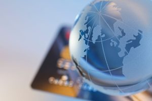 There is a glass globe of the world and a bank card under it on a table.