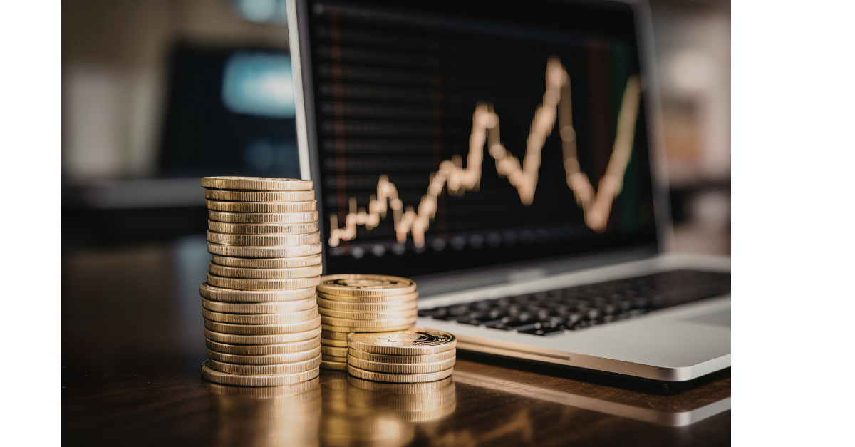 There are coins stacked up next to a laptop with a graph on the screen.
