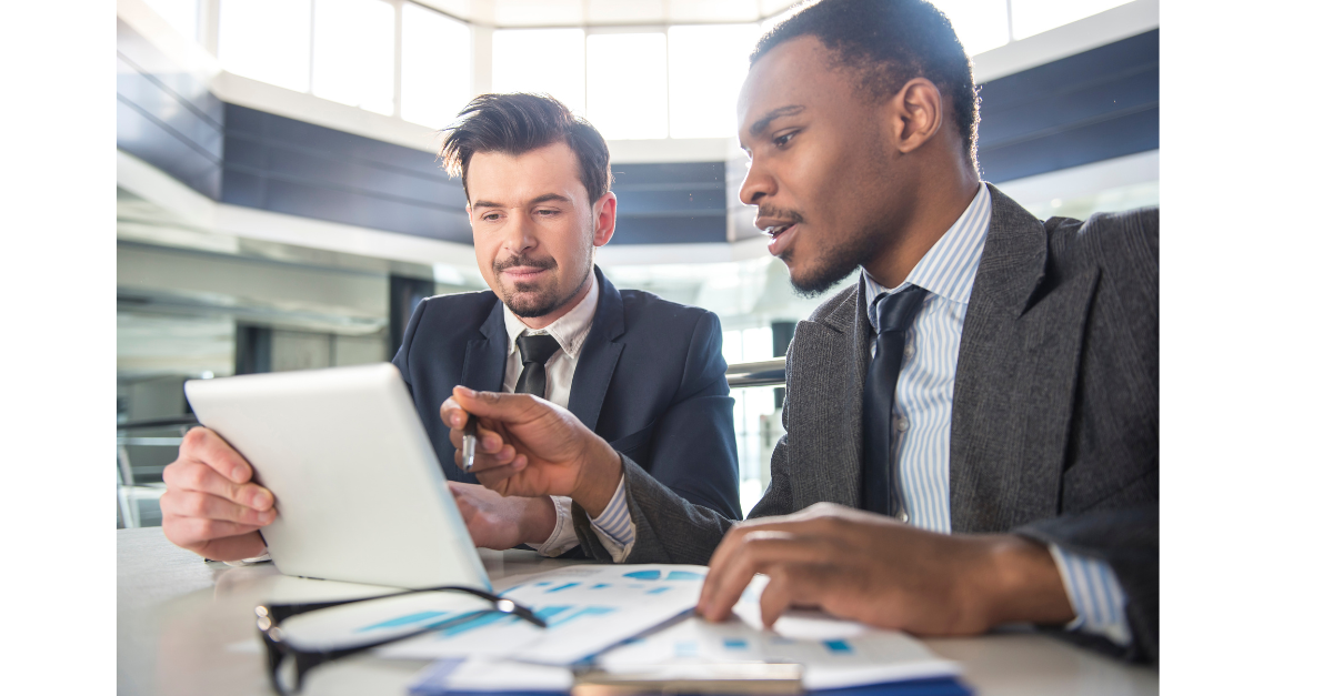 Two business men on a tablet with paper on clipboards and glasses on the office desk.