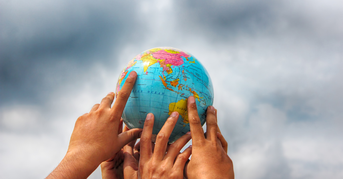 A group of peoples hands are holding up a globe high into the sky.