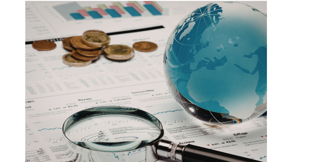 A glass globe on top of paper of charts, with coins and a magnifying glass.