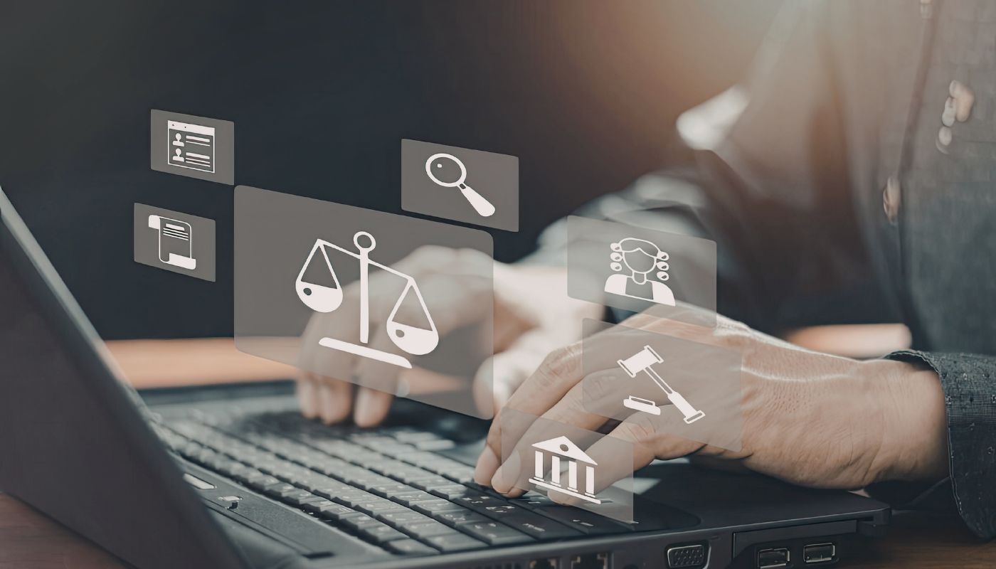 There is a man on a laptop typing on the keyboard with symbols above of weight scales, a gavel and magnifying glass