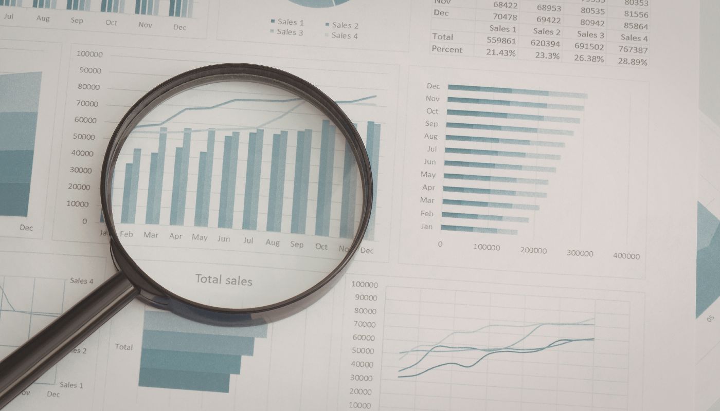 There is paper laid out with graphs and charts on and a magnifying glass across one of them.