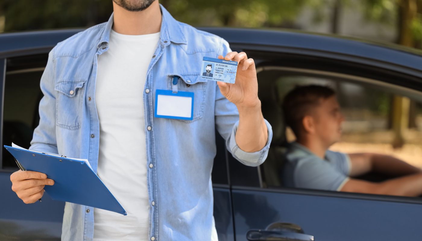 A man is holding a driving licence up in front of a car and holding a clipboard.