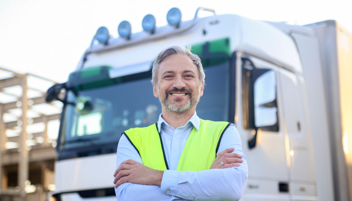 A man is standing outside his lorry wearing a hi-vis smiling.