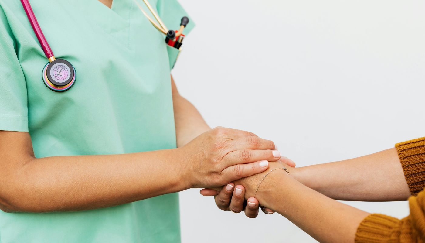 A nurse has a stethoscope around her neck and she is holding another women's hands.