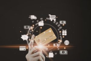 Someone holding a gold bank card with symbols around it of cash, a piggy bank, shopping bag and bank card.