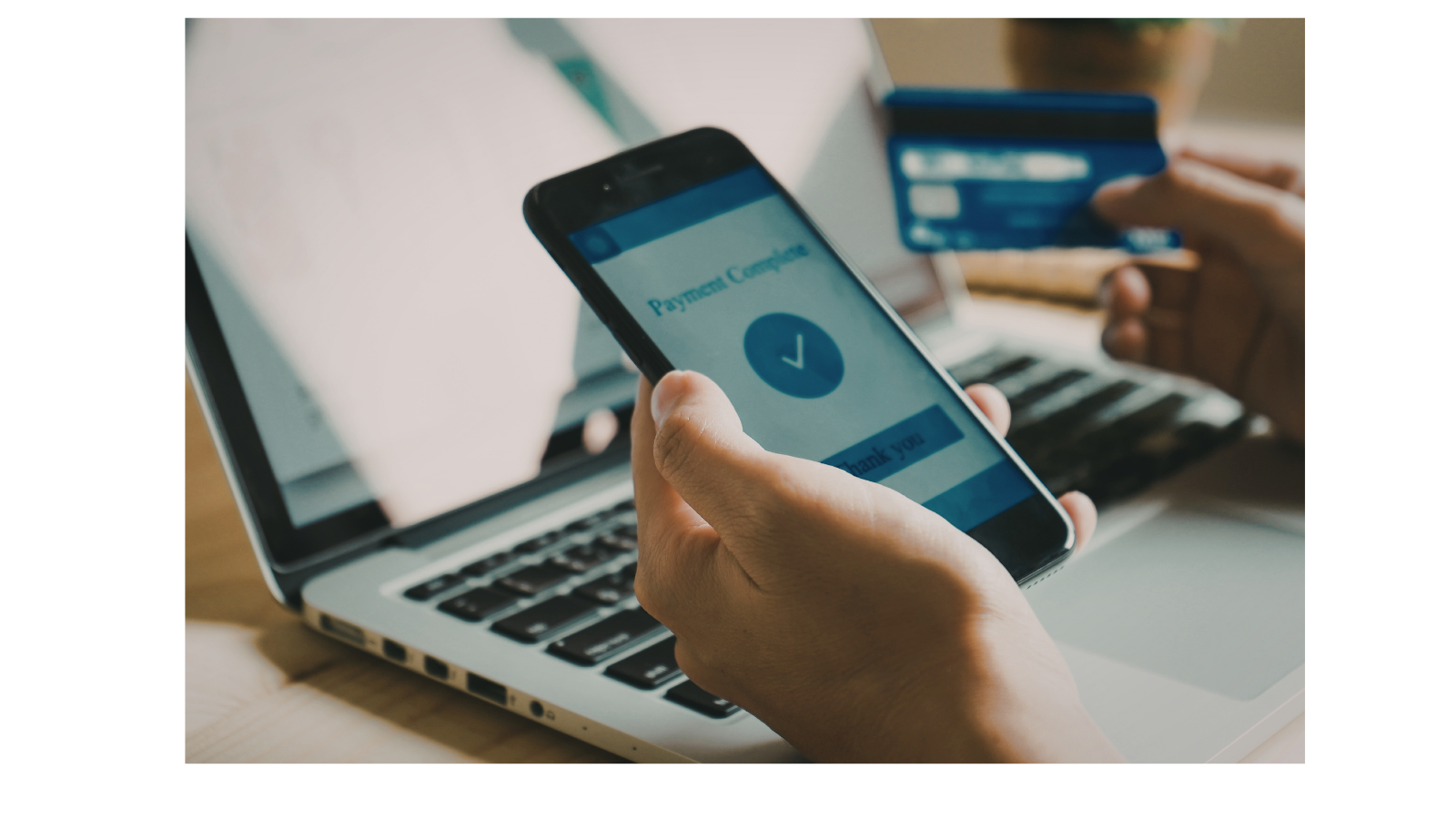 There is a phone open that says payment complete, a laptop and a bank card in someone's hand.