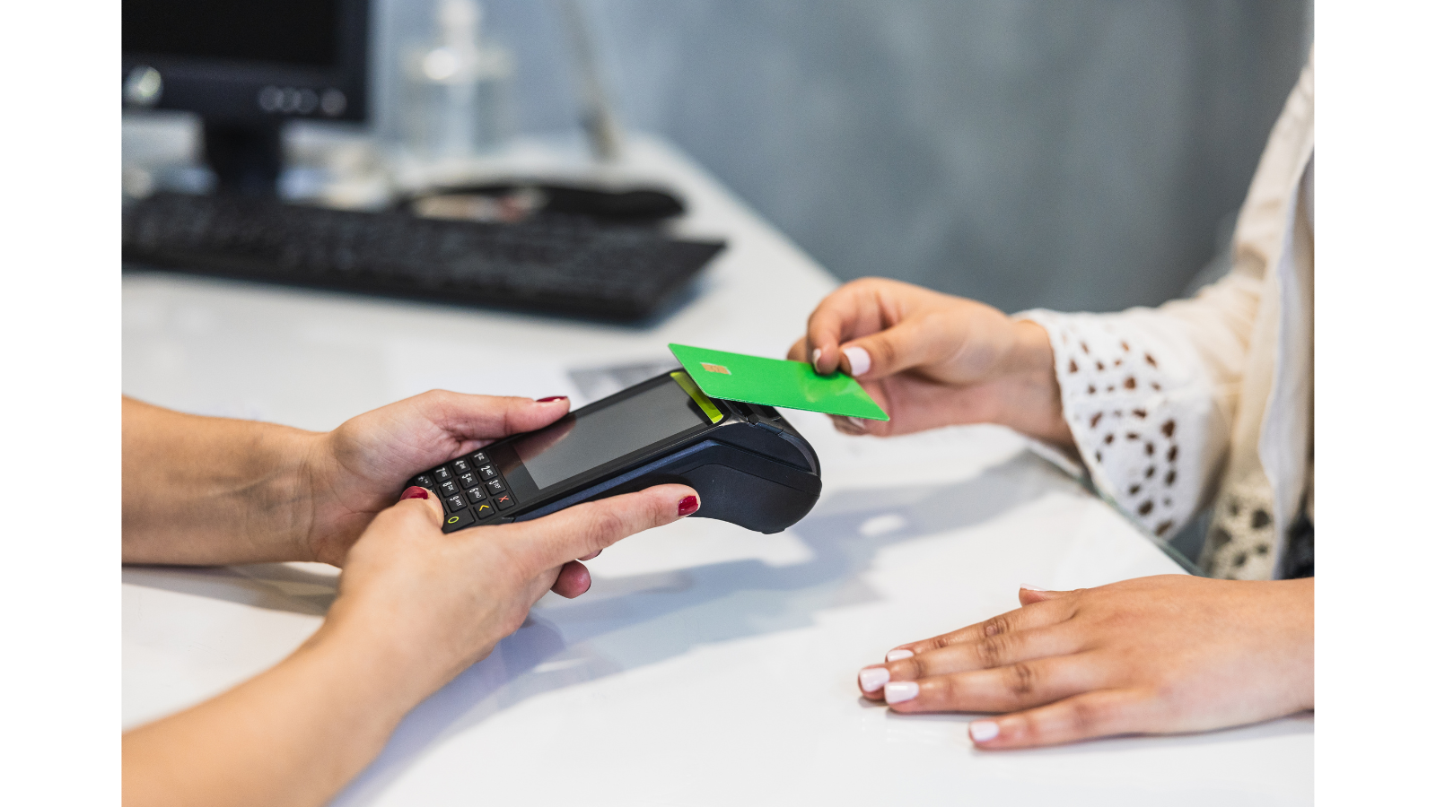 There is someone on one side of a desk with a card machine and another person on the other side with a bank card tapping it for contactless payment.