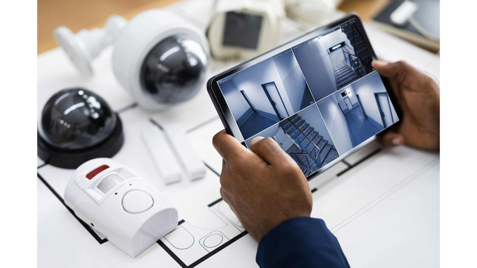 Someone is looking at a tablet of CCTV footage and there is a desk with cameras and alarms on.