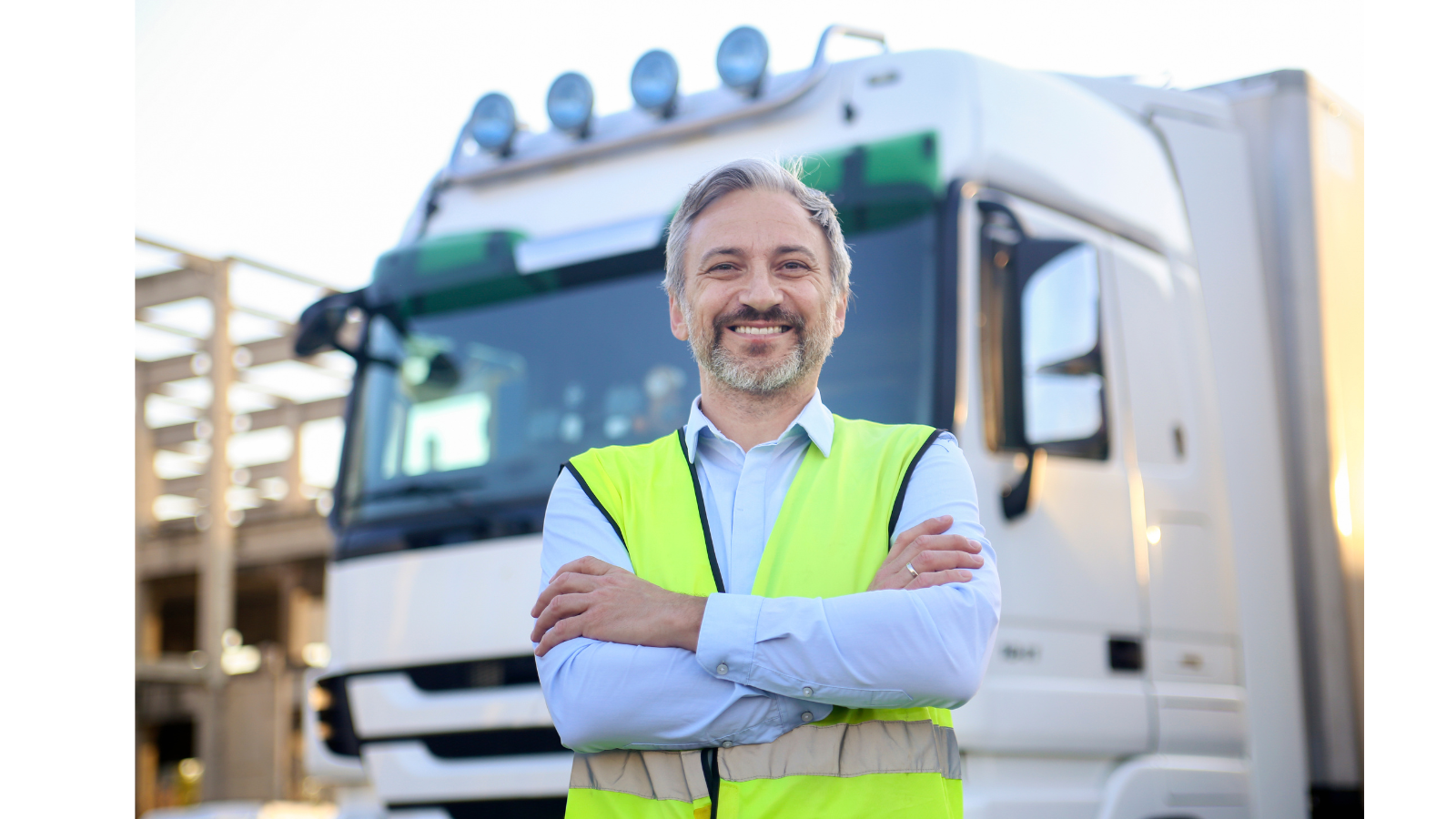 A man is standing outside his lorry wearing a hi-vis smiling.