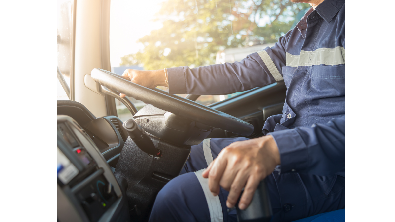 There is a man in overalls driving a lorry with a big steering wheel.