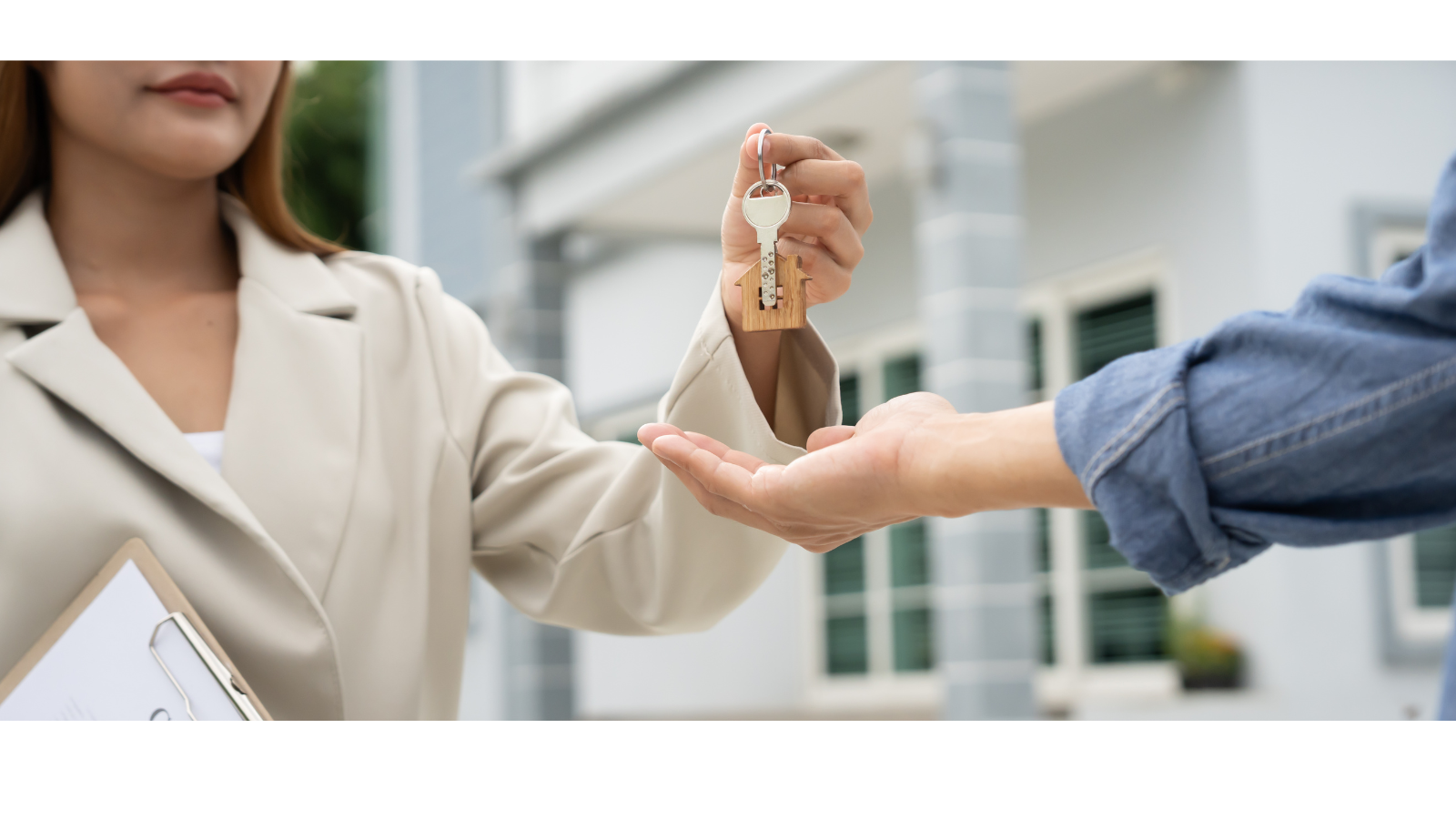 A lady wearing a blazer is handing over keys to someone with a clipboard under her arm.